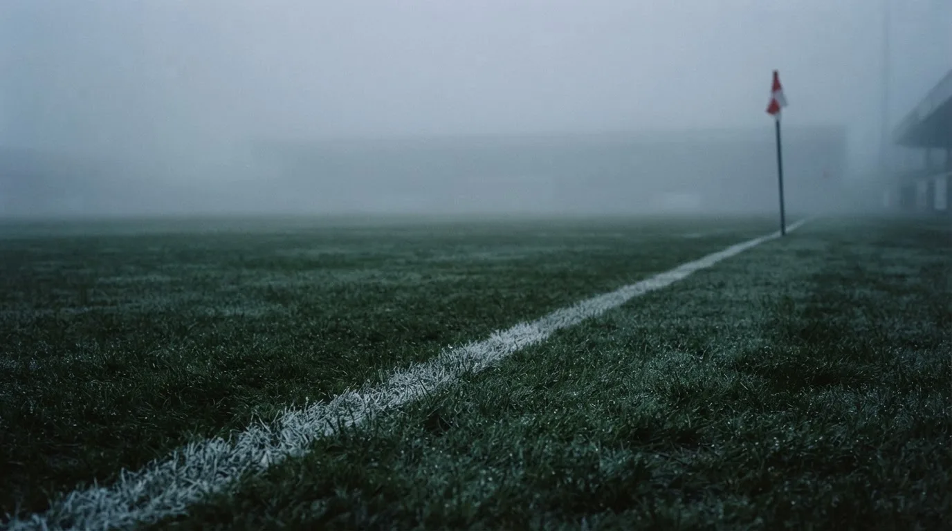 Der Rand eines Spielfelds mit weißer Linie und Eckfahne bei Nebel am frühen Morgen, ohne Menschen.