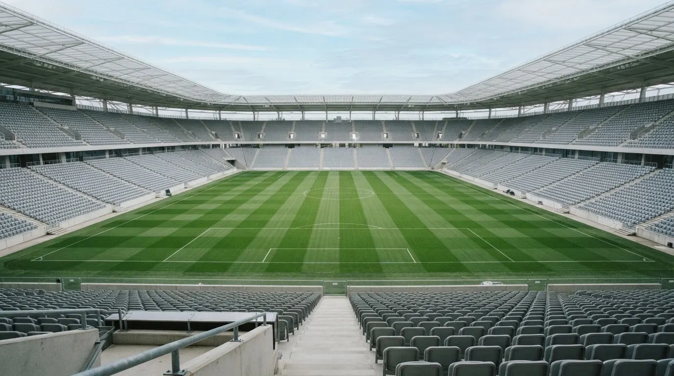 Ein leeres Fußballstadion bei Tageslicht von der Tribüne aus gesehen, der Rasen zeigt gleichmäßige Mähstreifen.
