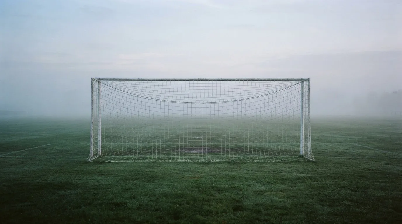 Ein Fußballtor mit Netz im Morgennebel auf einem leeren Platz, die Linien nur schwach zu erkennen.