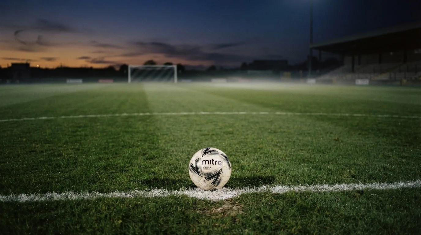 Ein Fußball liegt auf dem Elfmeterpunkt eines leeren Platzes im Abendlicht.