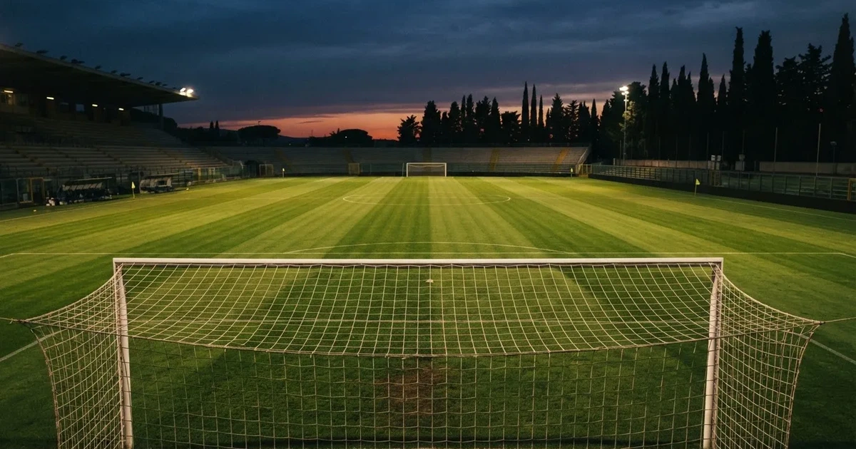 Ein Fußballtor mit Netz auf einem leeren Platz im Abendlicht, der Rasen frisch gemäht, im Hintergrund Zypressen.
