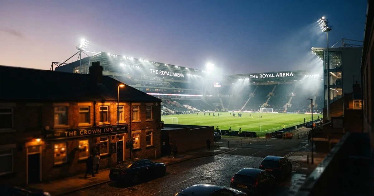 Ein Fußballstadion bei Flutlicht aus der Ferne gesehen, davor eine Straße und leuchtende Fenster eines Nebengebäudes.