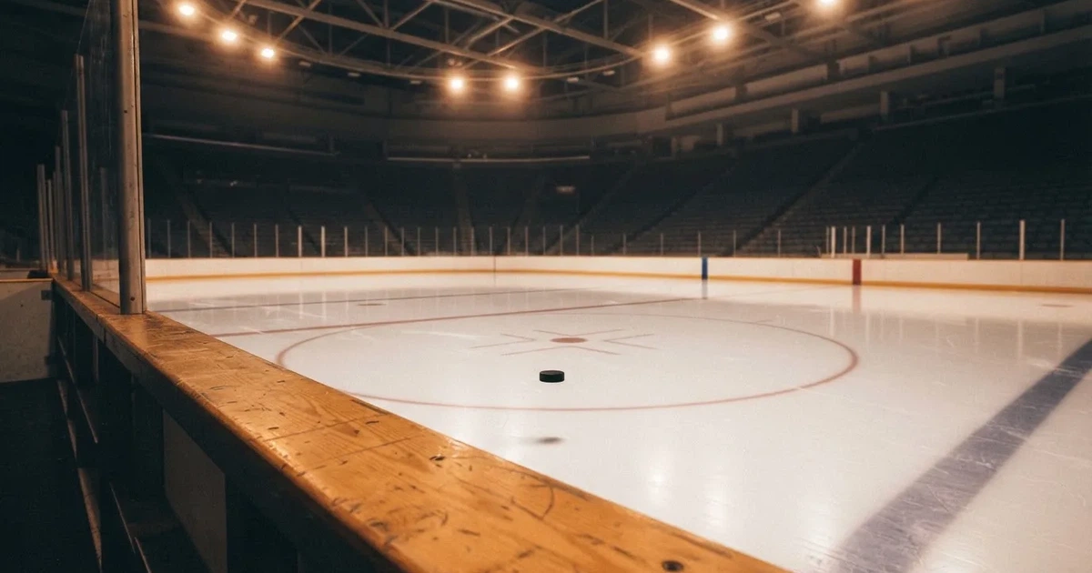 Eine leere Eisfläche in einer Halle mit Banden und Flutlicht, auf dem Eis liegt ein einzelner Puck.