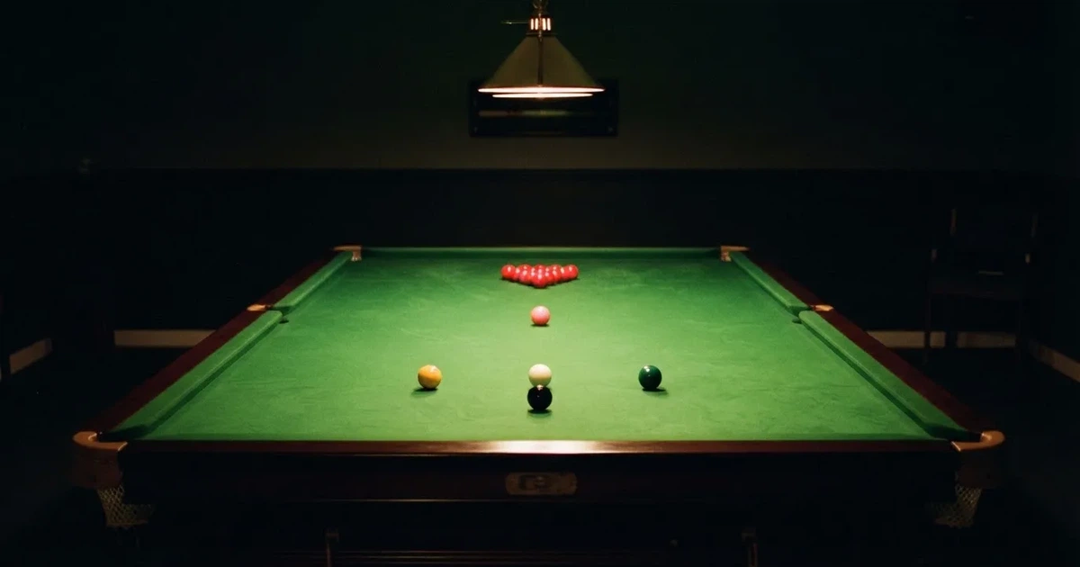 Ein Snookertisch mit grünem Tuch und aufgebauten roten Kugeln in einem abgedunkelten Raum unter einer hängenden Lampe.