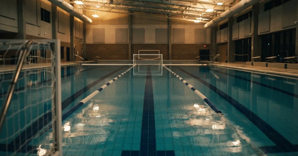 Ein Schwimmbecken mit türkisfarbenem Wasser und zwei schwimmenden Torrahmen am gegenüberliegenden Beckenrand, menschenleer unter Hallenlicht.