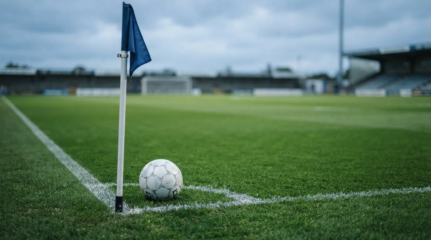 Ein Fußball liegt neben einer Eckfahne auf kurz gemähtem Rasen unter bewölktem Himmel.